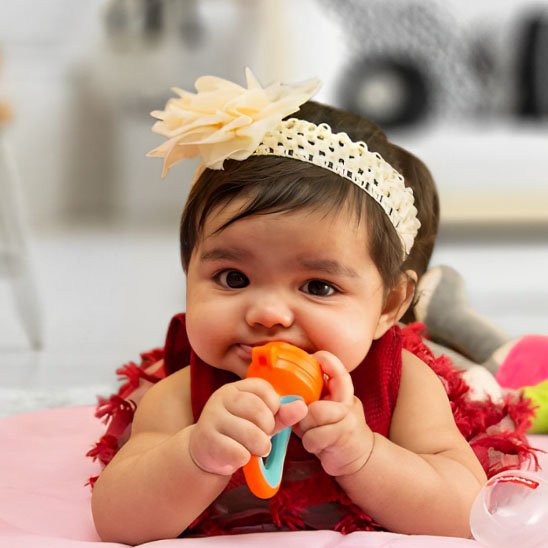 	Bébé fille mordant une grignoteuse colorée orange et bleue allongée – jouet de dentition premiers mois