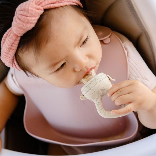 Bébé fille utilisant une grignoteuse silicone sans BPA dans une chaise haute – alimentation sécurisée