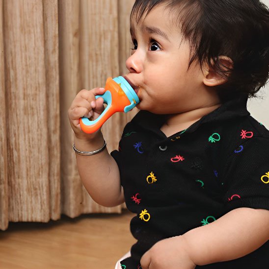 Bébé tenant une grignoteuse colorée orange et bleue – jouet de dentition pour premiers aliments
