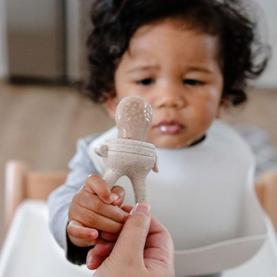 Grignoteuse bébé tenue par un parent présentée à un nourrisson en chaise haute – éveil sensoriel