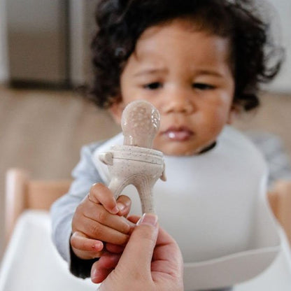 Grignoteuse bébé tenue par un parent présentée à un nourrisson en chaise haute – éveil sensoriel